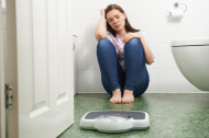 stock-photo-74105099-unhappy-teenage-girl-sitting-on-floor-looking-at-bathroom-scales